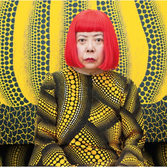 Yayoi Kusama posing in front of her yellow and black polka-dot pumpkin art