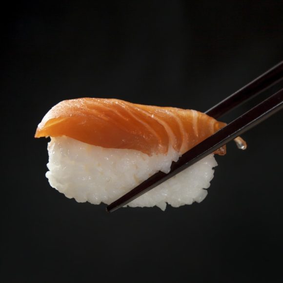 Salmon sushi with black chopsticks on a black background