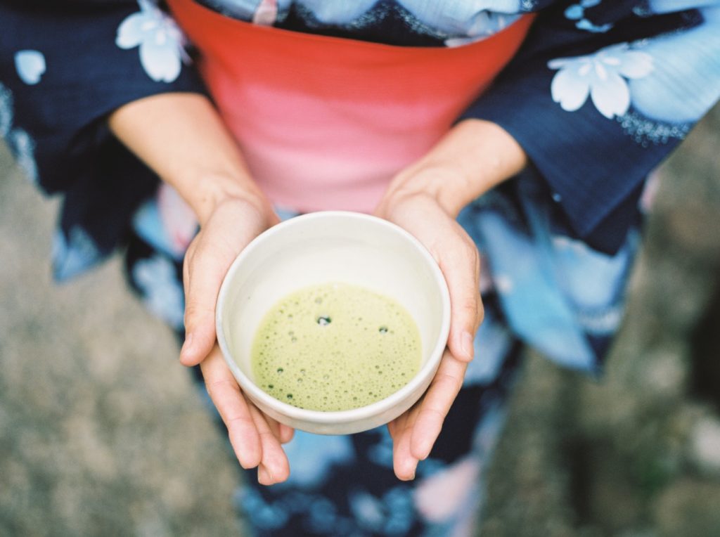 A Japanese woman wearing kimono holds a cup with matcha green tea